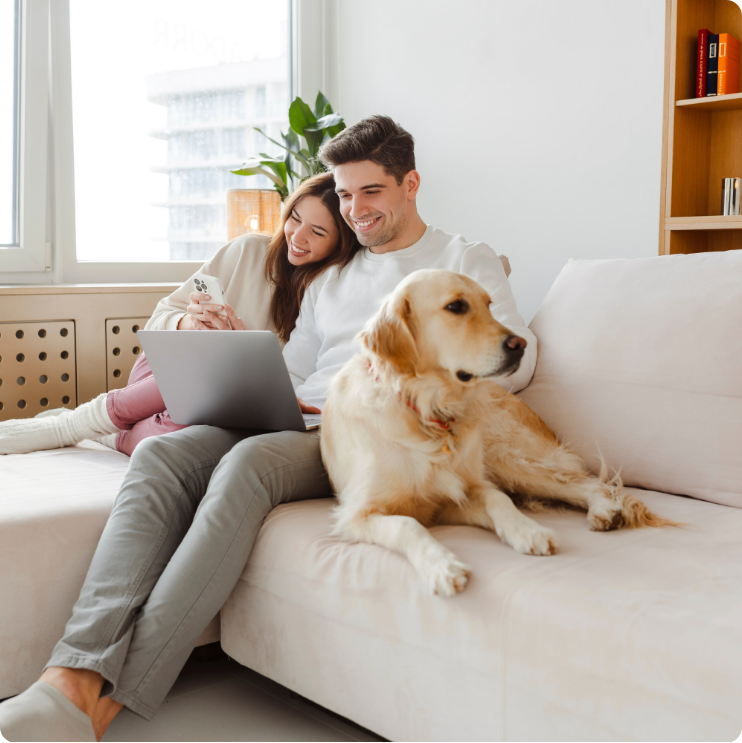 Man and woman looking at laptop while sitting on couch with their golden retriever