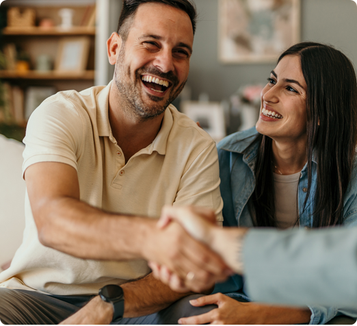 Man smiling and shaking hands with someone. Woman is looking at him and smiling. 