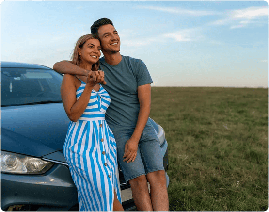 Happy couple leaning on car hood. 