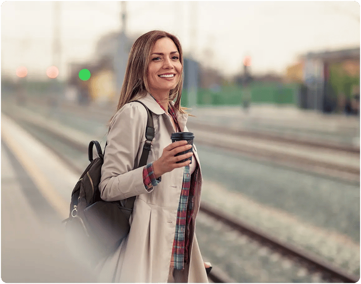 Girl standing near railroad tracks, with backpack on. Holding her phone and smiling. 